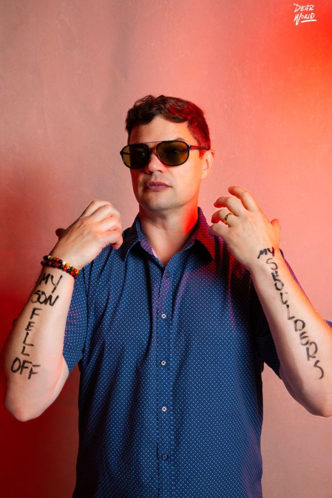 David Kolmer Brain Tatoo for Dear Wrold. A red back ground and red lights. and on Dave's arms reads "My Son Fell Off My Shoulders."